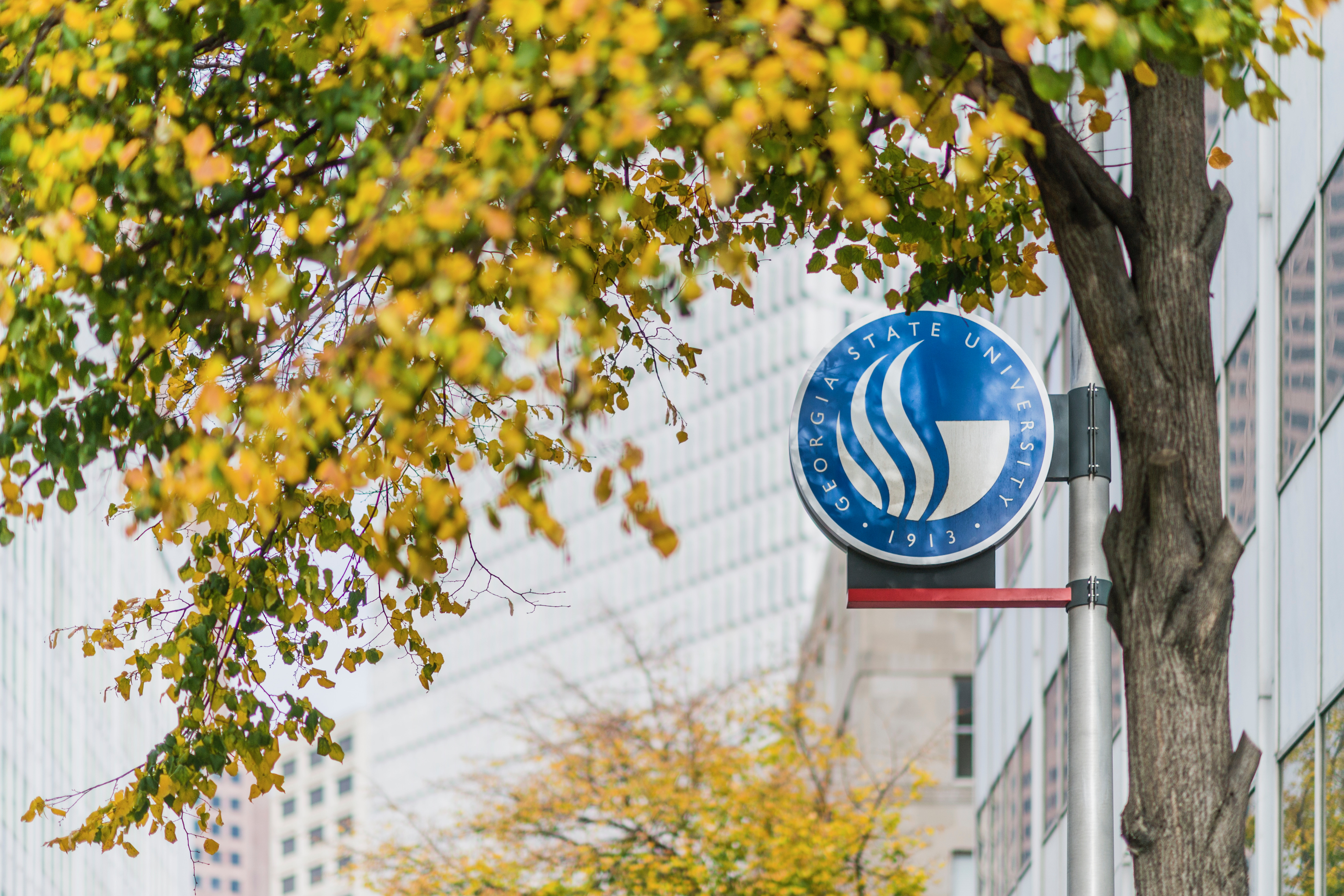 A Georgia State University seal bearing the 1913 founding year on a downtown campus lamppost, framed by golden autumn leaves