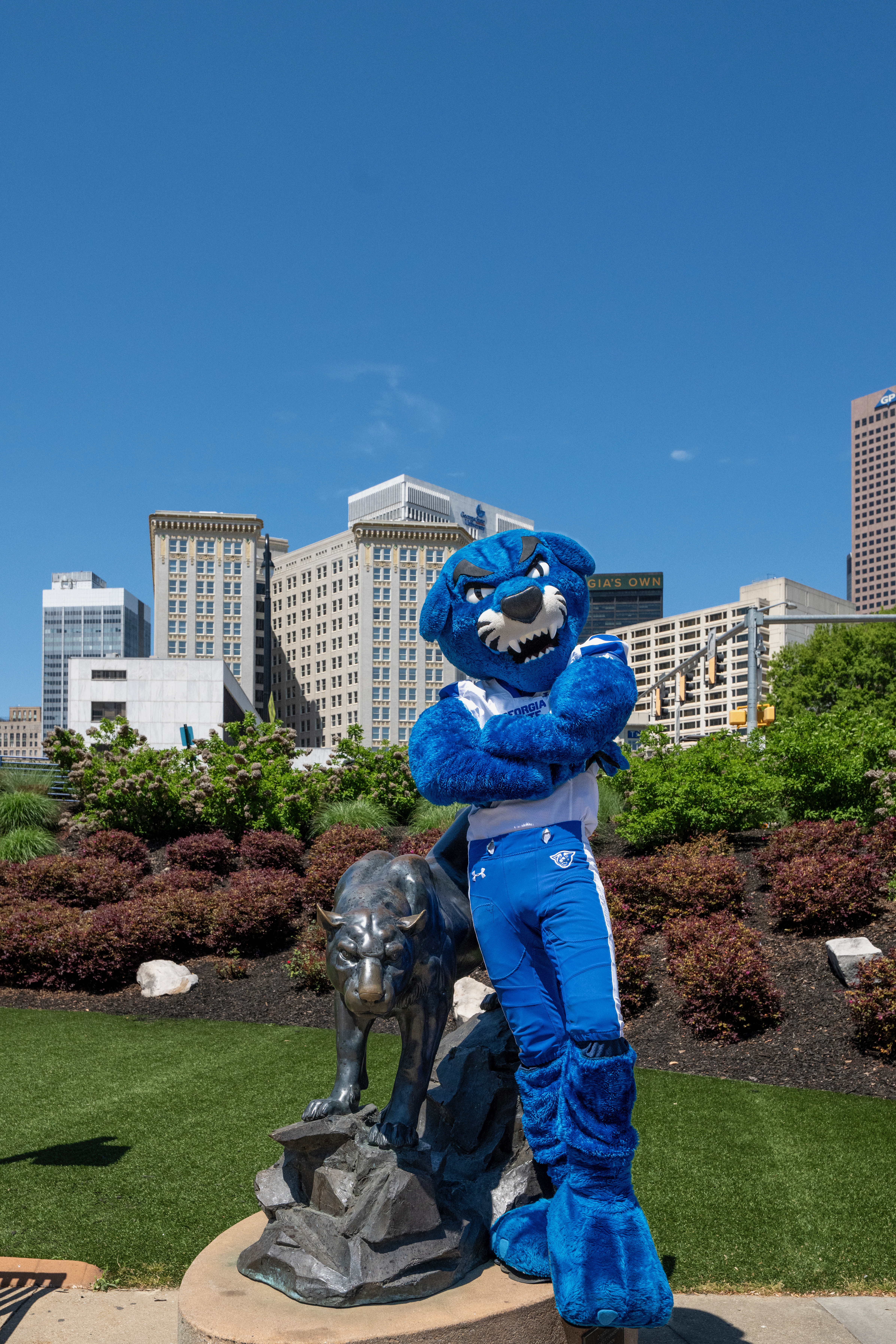 Pounce, the Georgia State University panther mascot, posing beside the bronze panther statue with the downtown Atlanta skyline behind