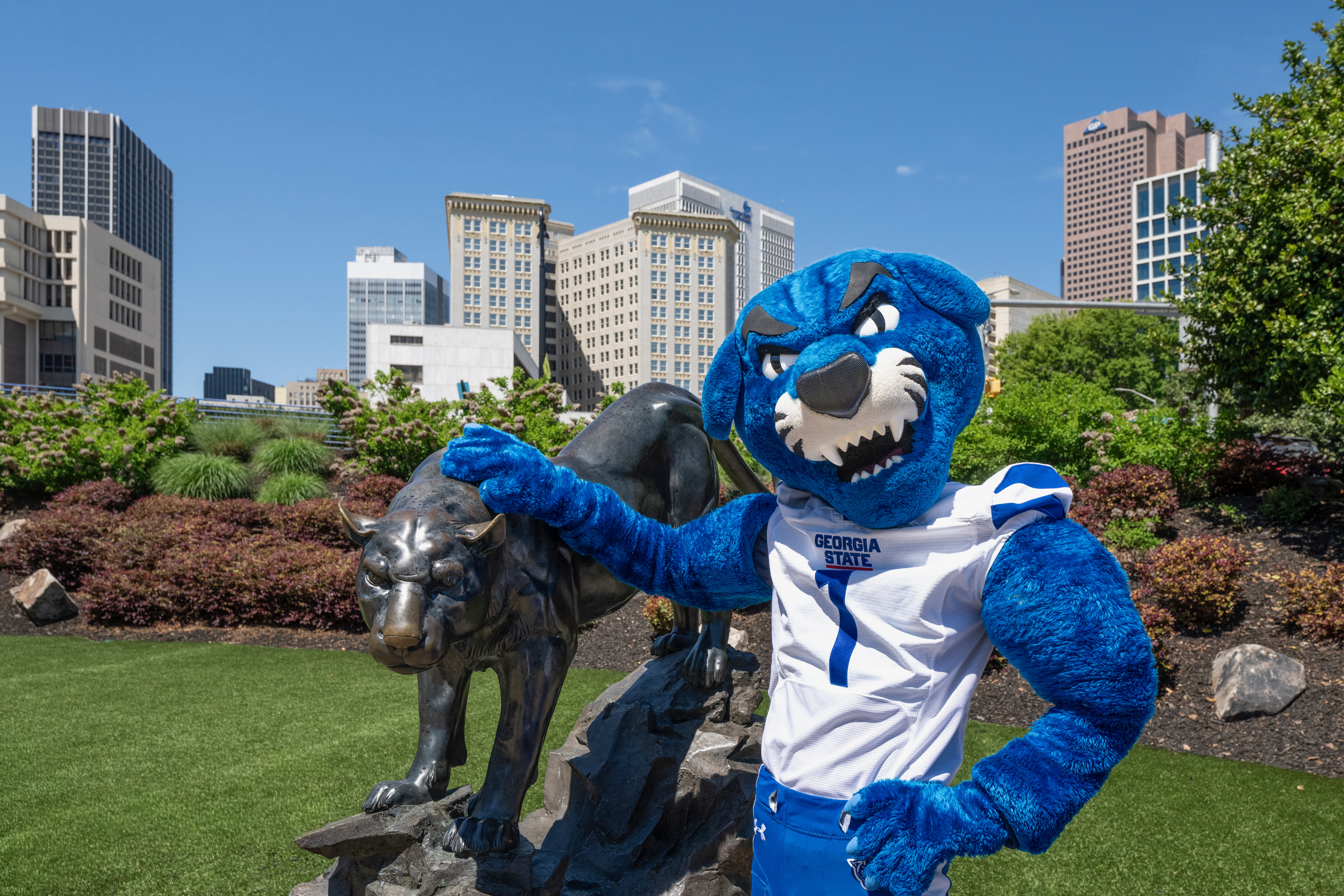Pounce, the Georgia State University panther mascot, posing beside the bronze panther statue with the downtown Atlanta skyline behind